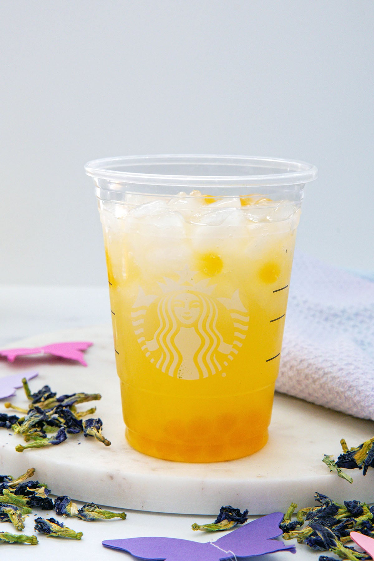 Head-on view of a Starbucks cup filled with mango boba, tropical butterfly Refresher base, and water with ice.