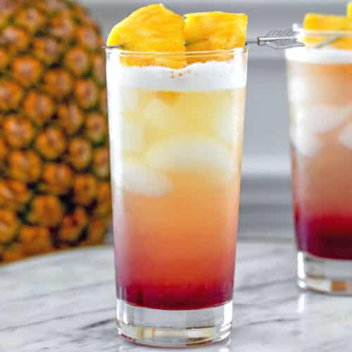 Closeup view of a layered tropical gin sunrise drink with pineapple in background.