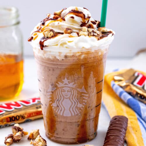 Head-on closeup view of a Twix Frappuccino with whipped cream, caramel, and mocha sauce, with Twix bars in the background