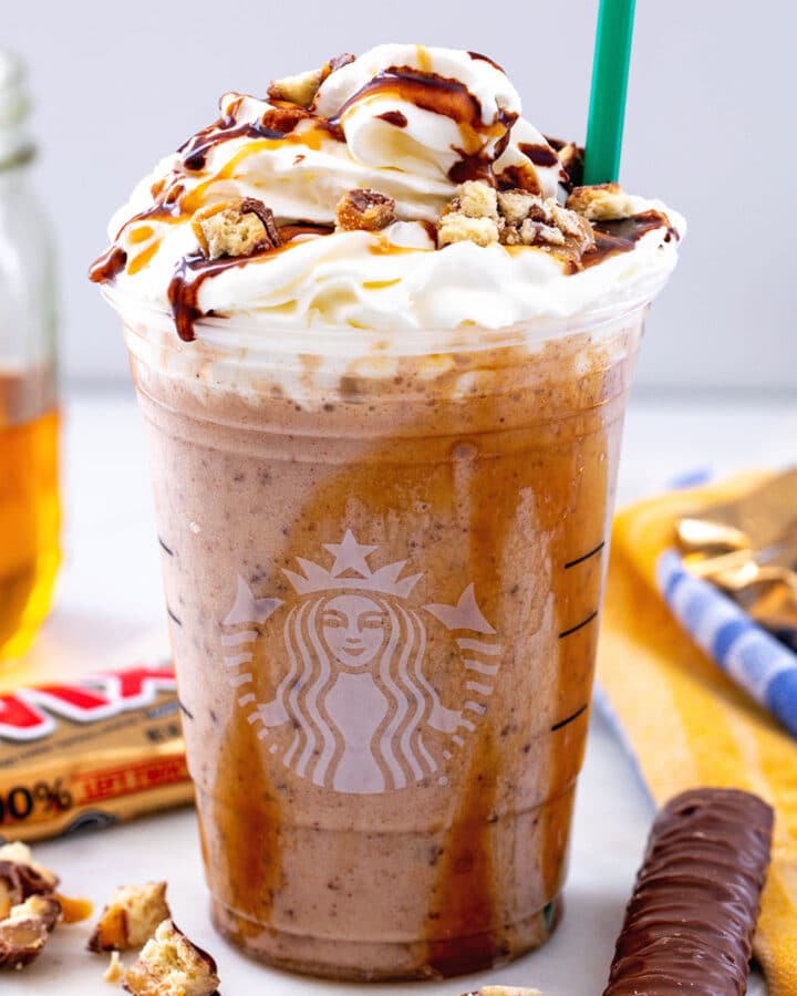 Head-on closeup view of a Twix Frappuccino with whipped cream, caramel, and mocha sauce, with Twix bars in the background
