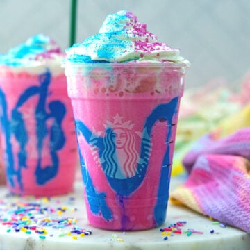 Closeup view of a bright pink Unicorn Frappuccino with blue drizzles and whipped cream on top.
