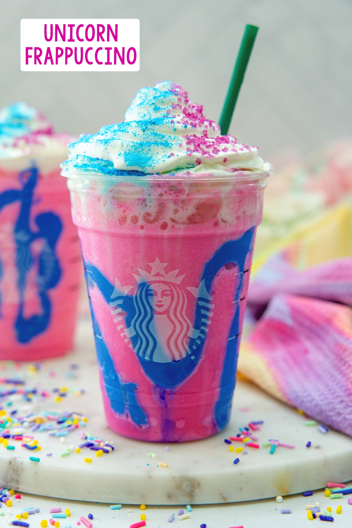 Head-on view of the Unicorn Frappuccino, a magenta drink with blue drizzle with whipped cream, sprinkles all around, and recipe title at top.