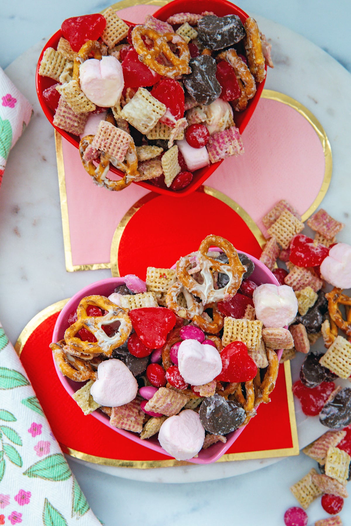Two heart-shaped bowls on heart napkins filled with Valentine snack mix.