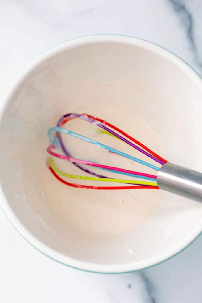 Vanilla icing in mixing bowl with rainbow whisk.