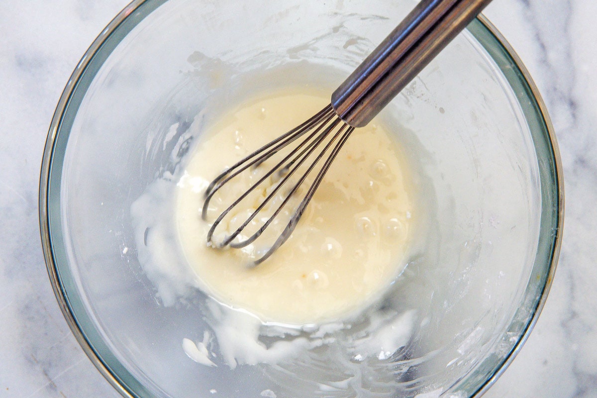 Vanilla icing in bowl with whisk.
