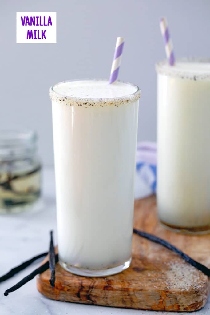 Head-on view of a tall glass of vanilla milk with second glass and jar of vanilla syrup in background and recipe title at top.