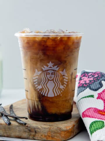 Head-on view of a Vanilla Sweet Cream Cold Brew with vanilla beans on side and jar of sweet cream in background.