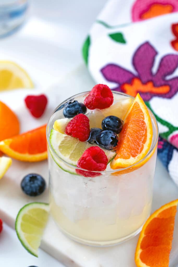 Overhead view of a vodka soda topped off with raspberries, blueberries, lime wedges, and orange wedges.