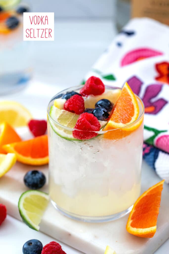 Vodka seltzer drink in a glass with berries and orange and lemon slices with recipe title at top.
