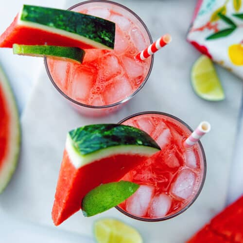 Overhead view of two watermelon refreshers in glasses with garnish.