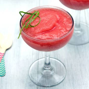 Closeup view of pink watermelon rosé slush in a glass with lime zest garnish.