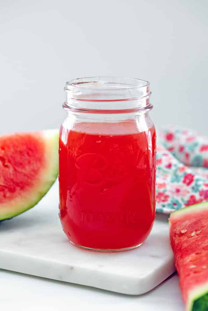 Watermelon syrup in jar with watermelon slices around.