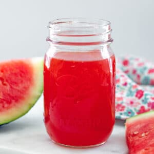 Closeup of a mason jar of watermelon syrup with slices of watermelon next to it.