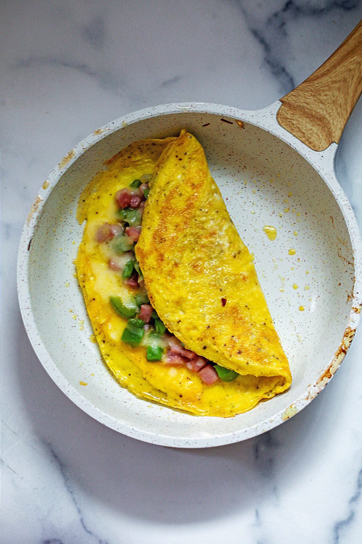 Omelet folded over in skillet with green pepper, ham, onion, and melted cheese peeking out.