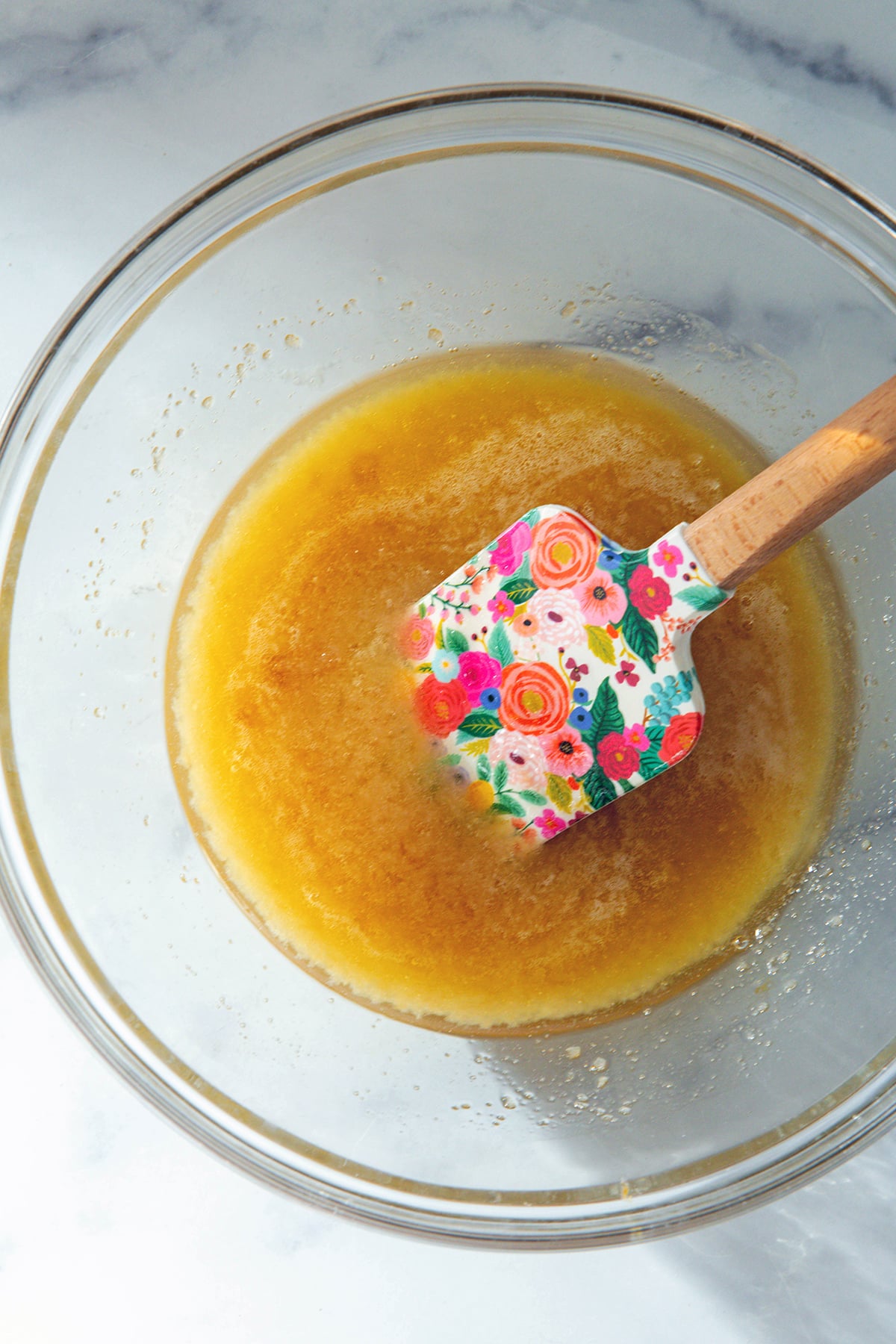 Eggs, oil, wet ingredients in bowl with floral spatula.