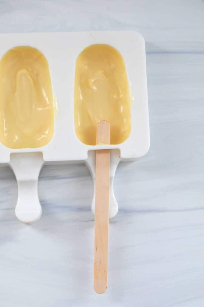 Melted white chocolate in cakesicle mold with popsicle stick.