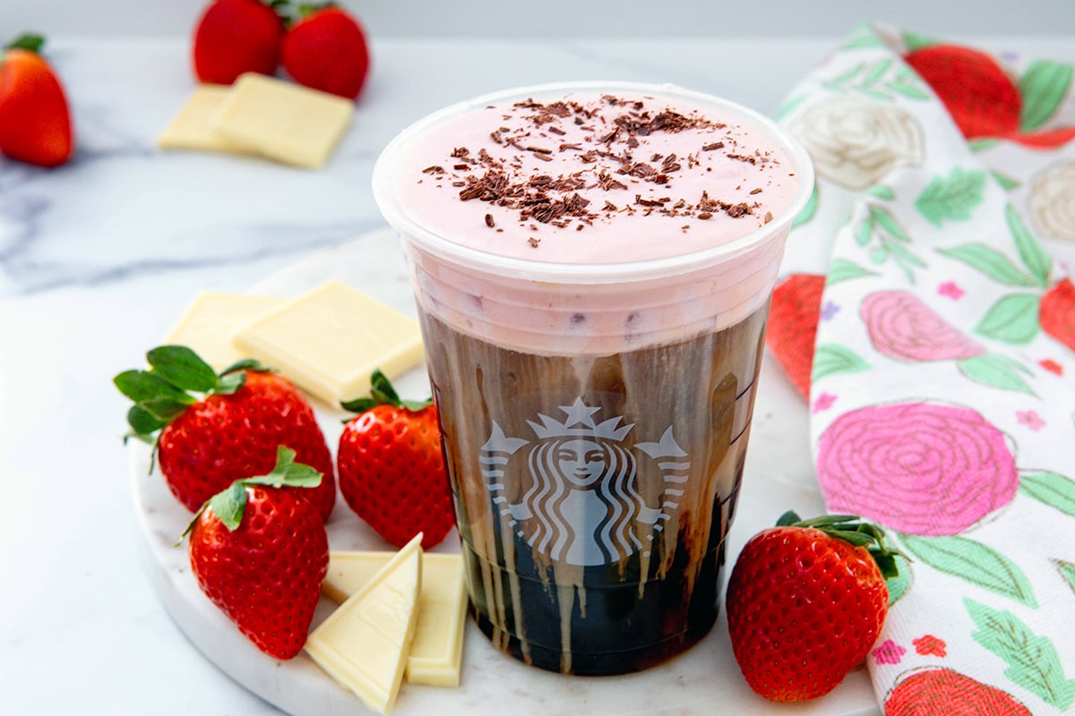 Overhead landscape photo of a White Chocolate Strawberry Cream Cold Brew with white chocolate bars and strawberries all around.