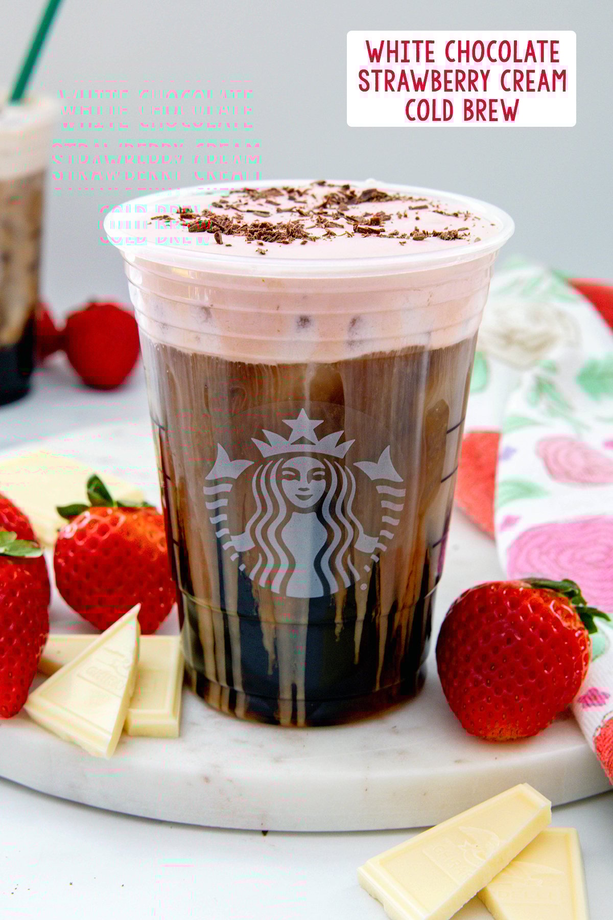 White Chocolate Strawberry Cream Cold Brew in a Starbucks cup with chocolate shavings on top, strawberries and white chocolate in background, and recipe title at top.