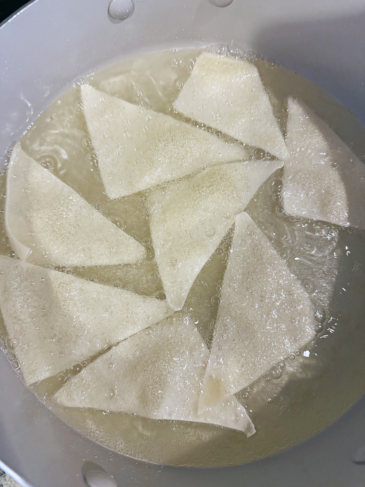 Wonton wrapper triangles frying in oil.