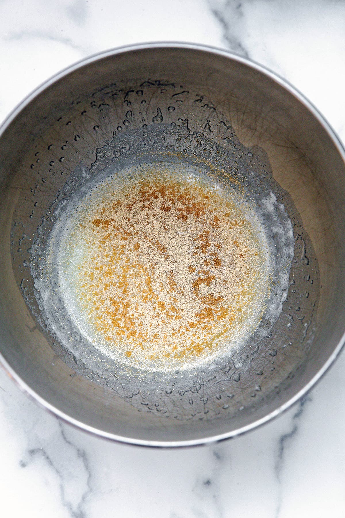 Warmed milk in mixing bowl with yeast sprinkled over it.