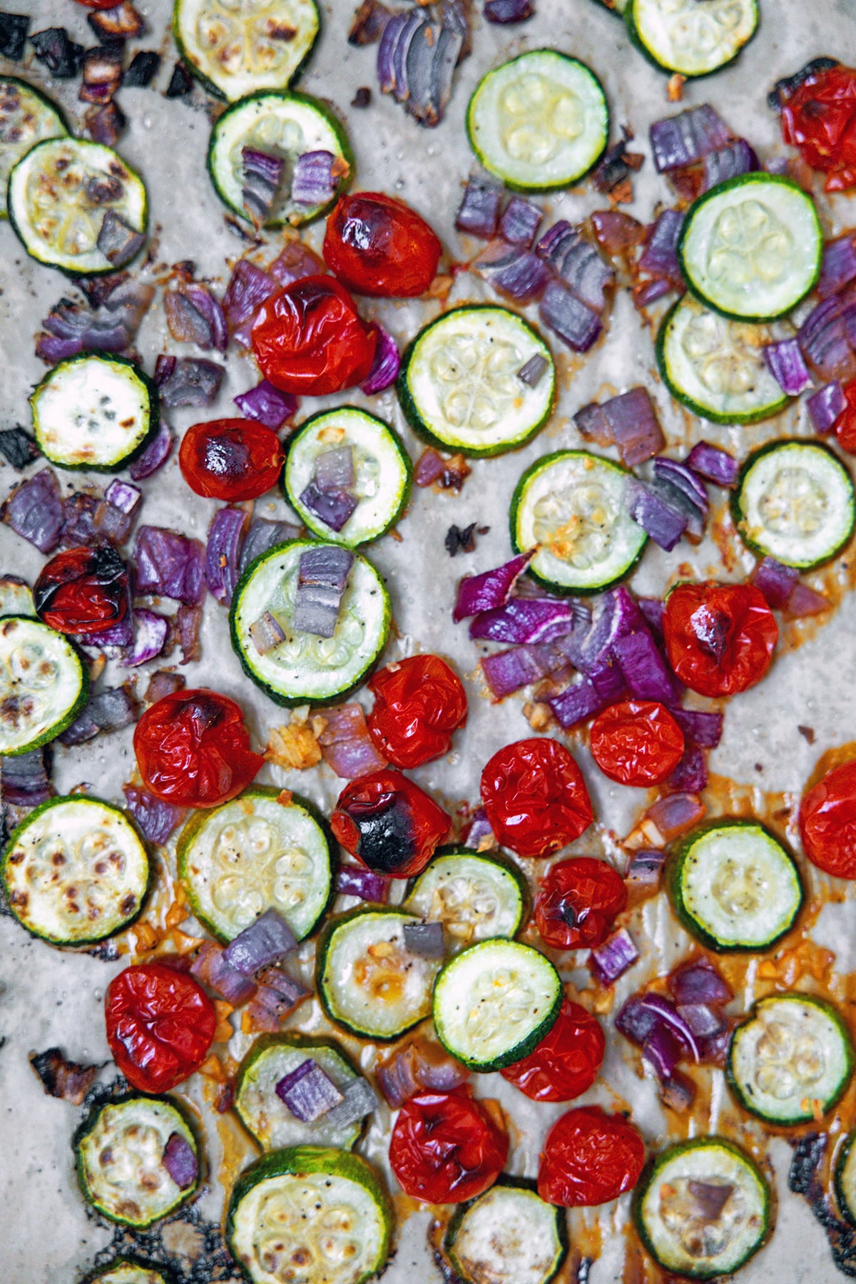 Roasted zucchini, tomatoes, and red onion on baking sheet.
